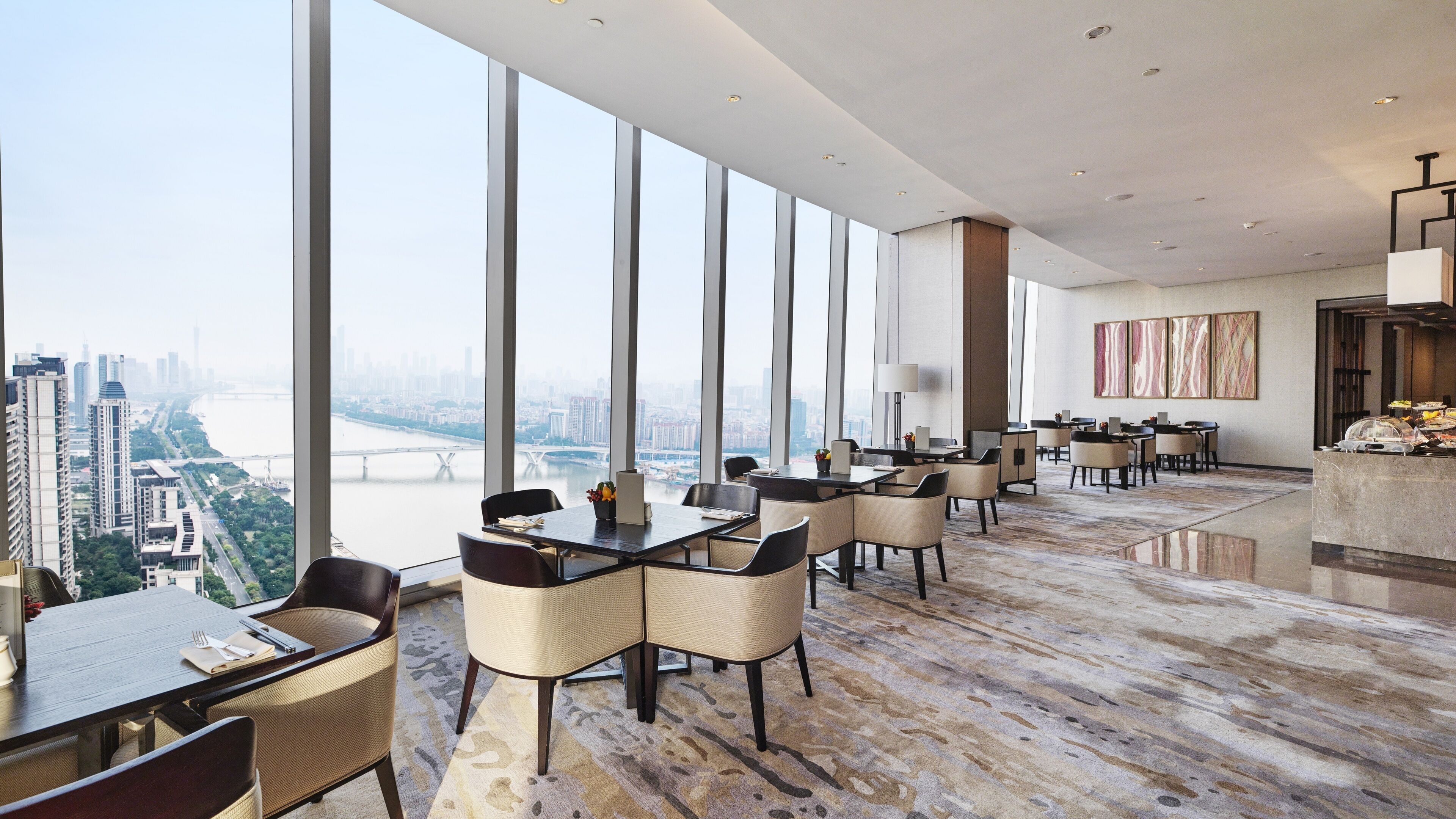 A modern dining area with high ceilings and large windows offering a city view.
