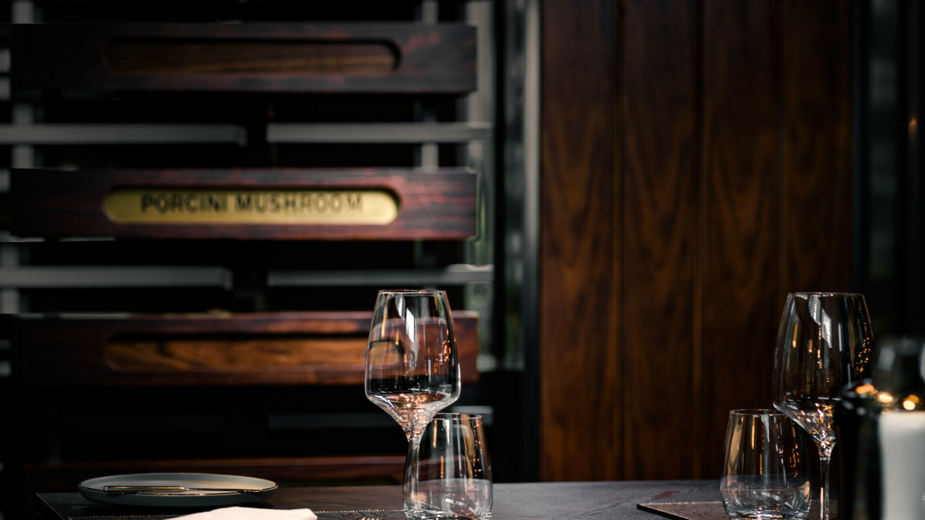 A dining table with empty wine glasses and a menu sign reading 'PORCINI MUSHROOM'.
