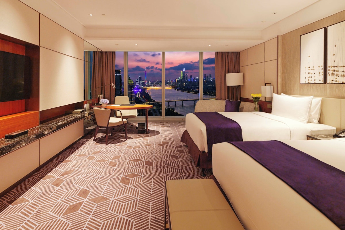 Habitación de hotel con cama, escritorio, silla, televisión y vista a la ciudad.