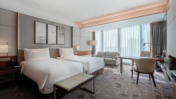 A hotel room with two beds, a desk, a chair, and a large window with curtains.