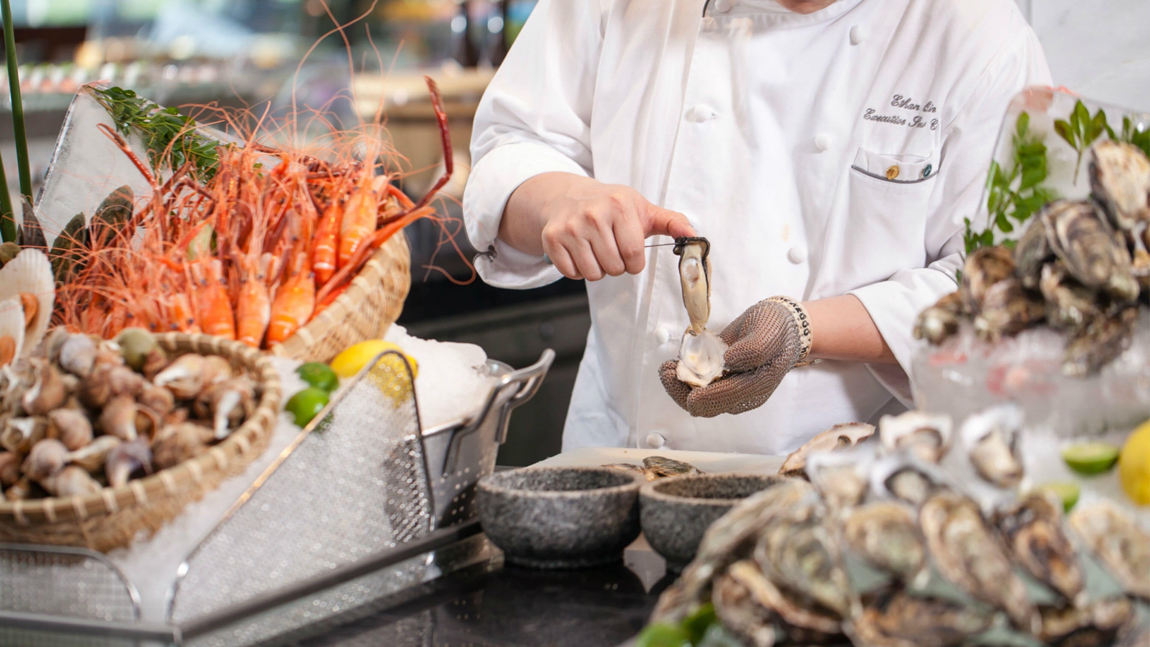 Un chef préparant des fruits de mer, entouré de différents types de fruits de mer et d’ustensiles de cuisine.
