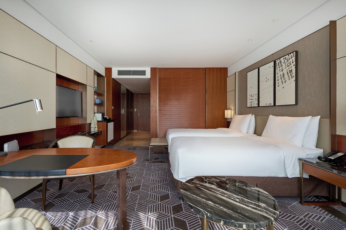 A hotel room with a bed, bedside table, desk, chair, and a TV.