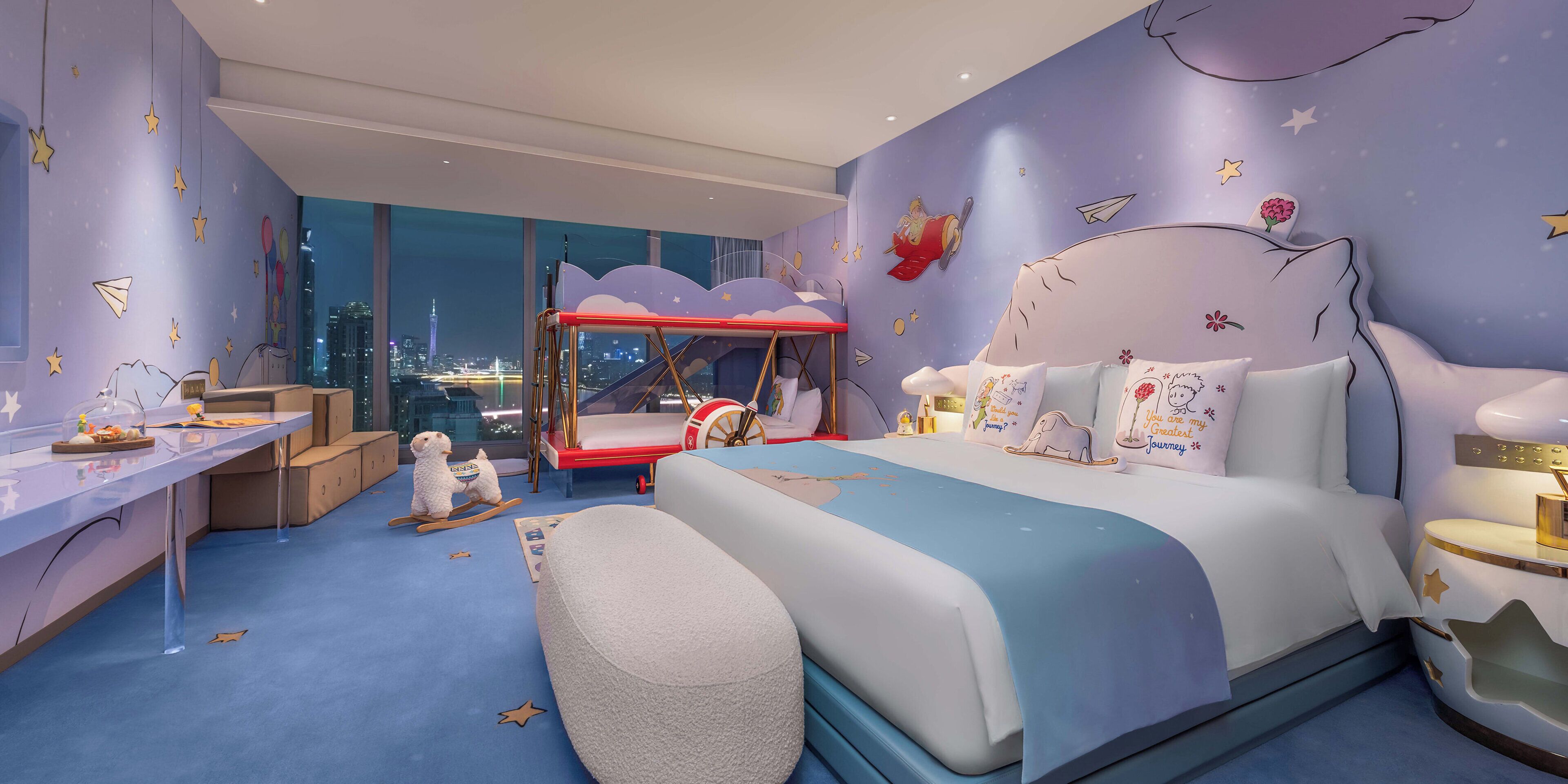 A child's bedroom with a bunk bed, a desk, and a view of the cityscape.