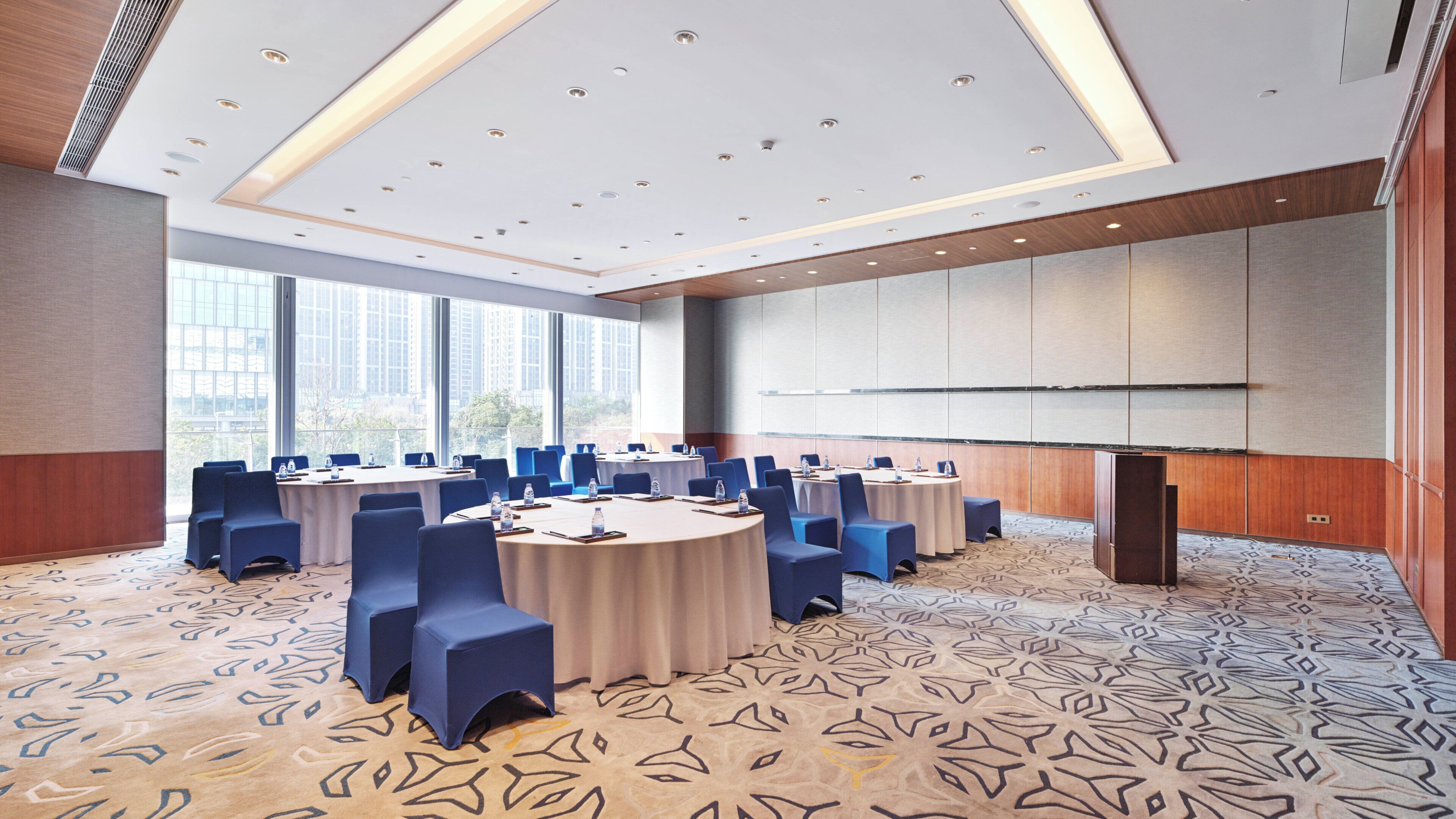 A conference room with round tables, blue chairs, and a patterned carpet.