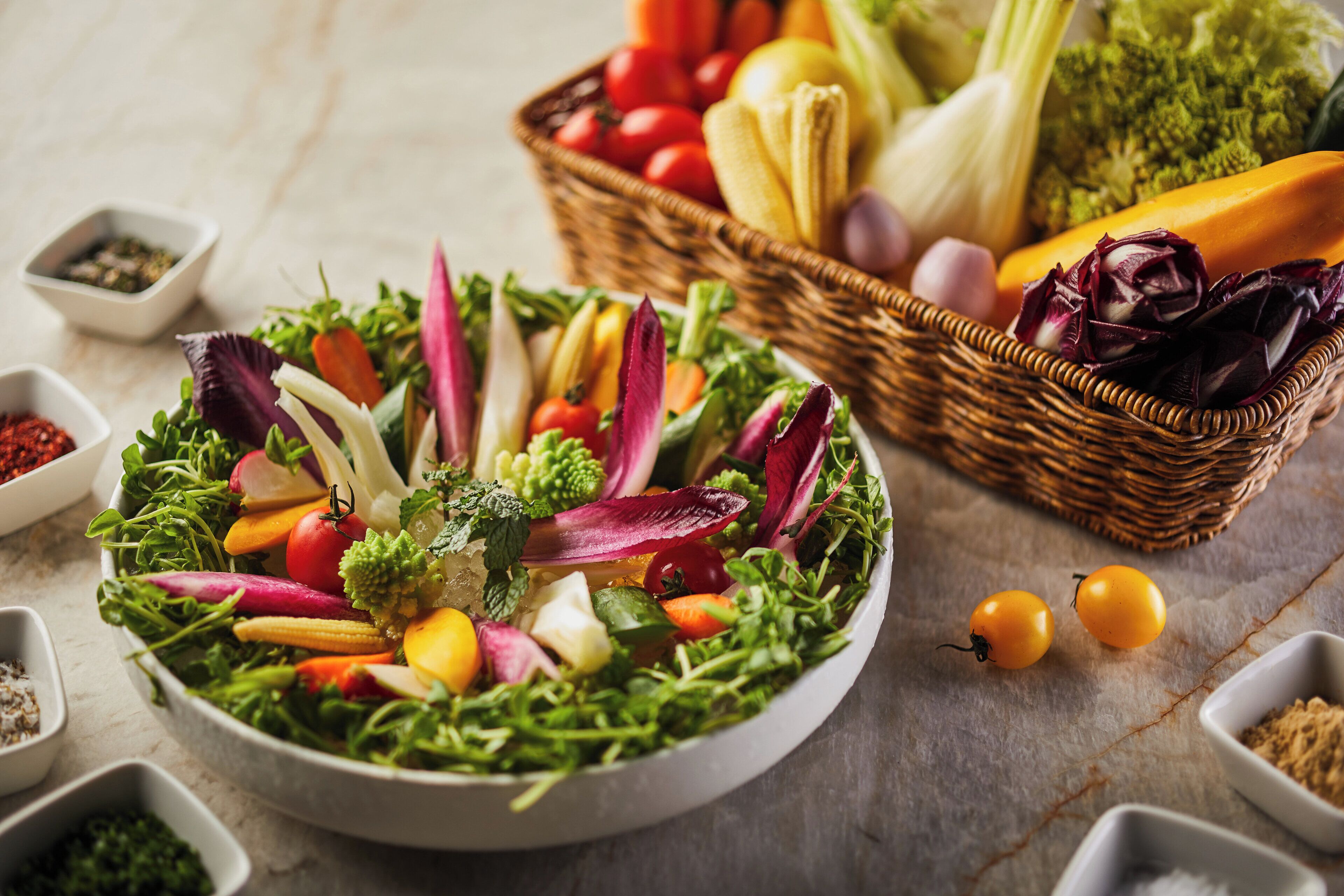 A salad bowl with various vegetables and a basket of fruits and vegetables in the background.