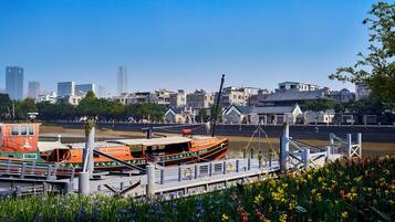 A riverfront with a traditional boat docked, a bridge, and a cityscape with modern buildings in the background.
