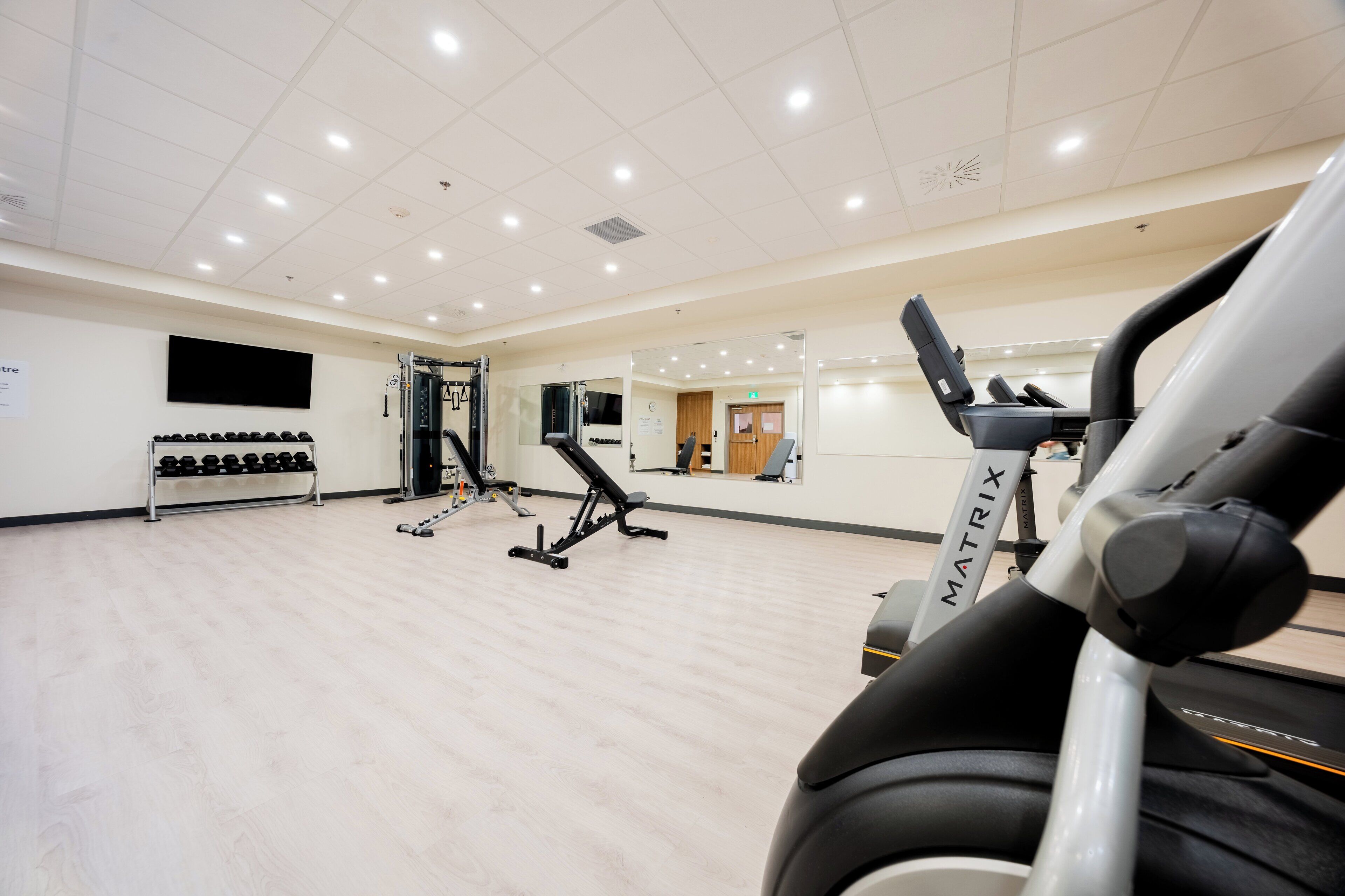 A gym with exercise equipment, a treadmill, and a wall-mounted TV.