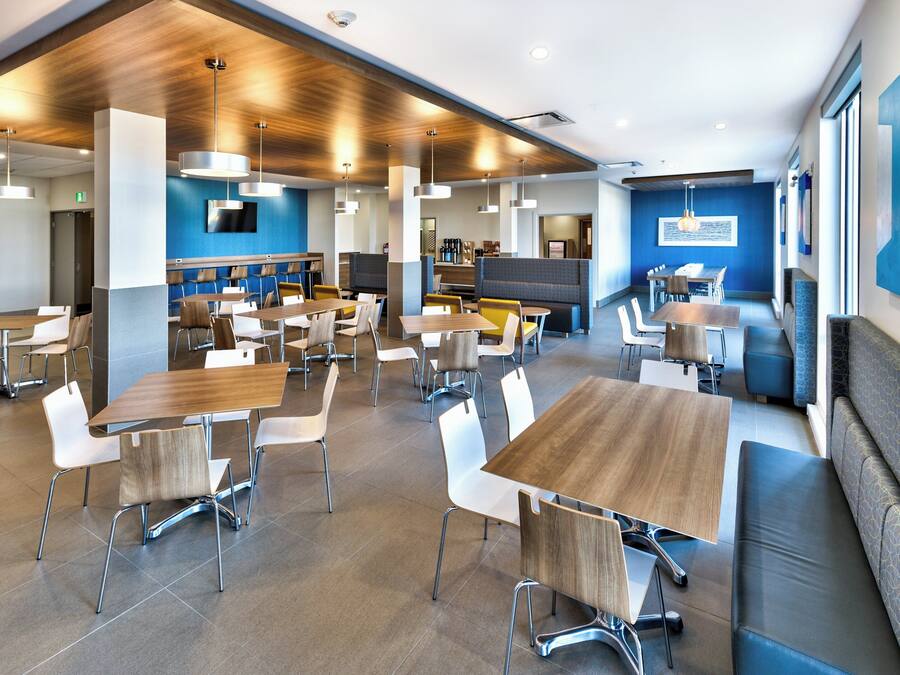 A modern dining area with multiple tables and chairs, a counter with a coffee machine, and a blue accent wall.