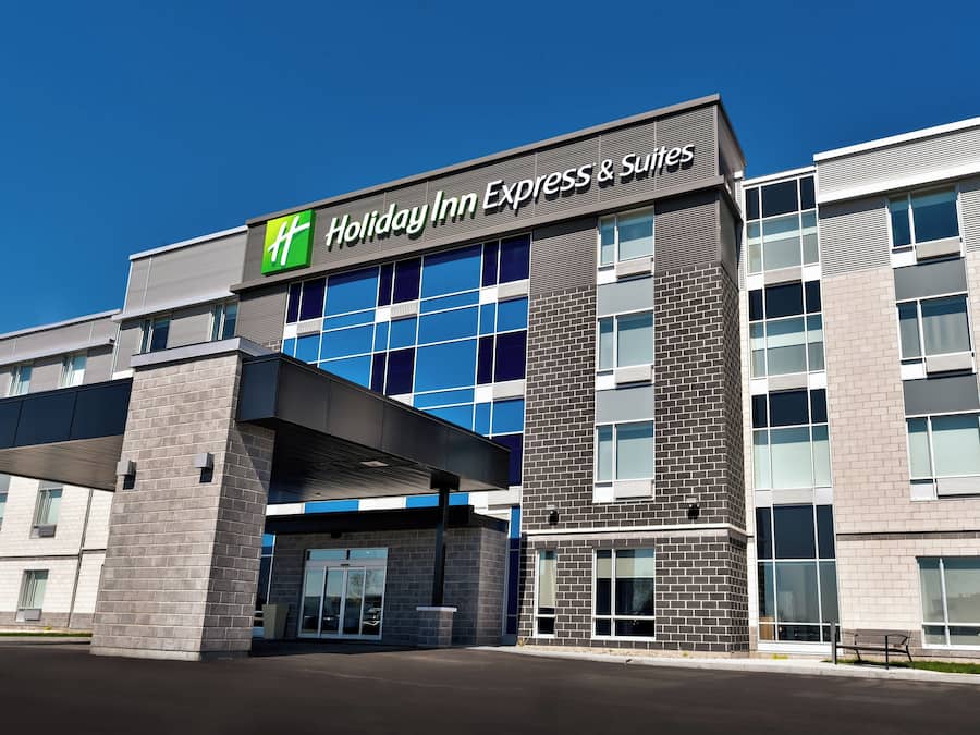 A Holiday Inn Express & Suites building with a modern architectural design, featuring a prominent entrance and a clear sky above.