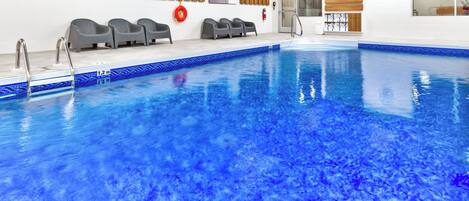 A swimming pool with a 1.2m depth marker, grey lounge chairs, and wooden panel decor.