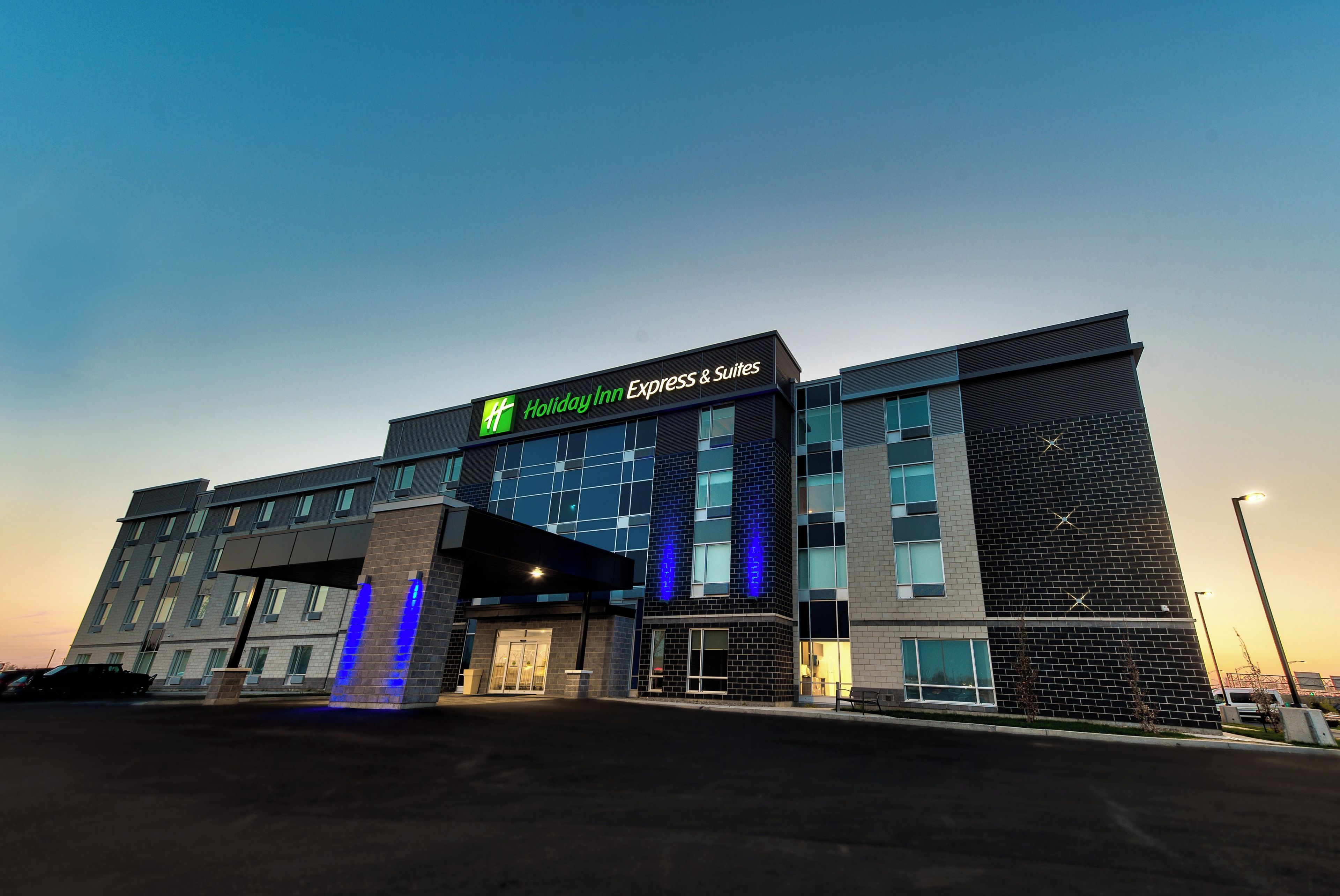A Holiday Inn Express & Suites hotel with a modern design, featuring a prominent sign and a well-lit entrance.