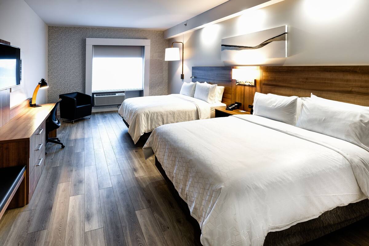 Habitación de hotel con dos camas, un escritorio con lámpara, una silla y un ventanal grande.