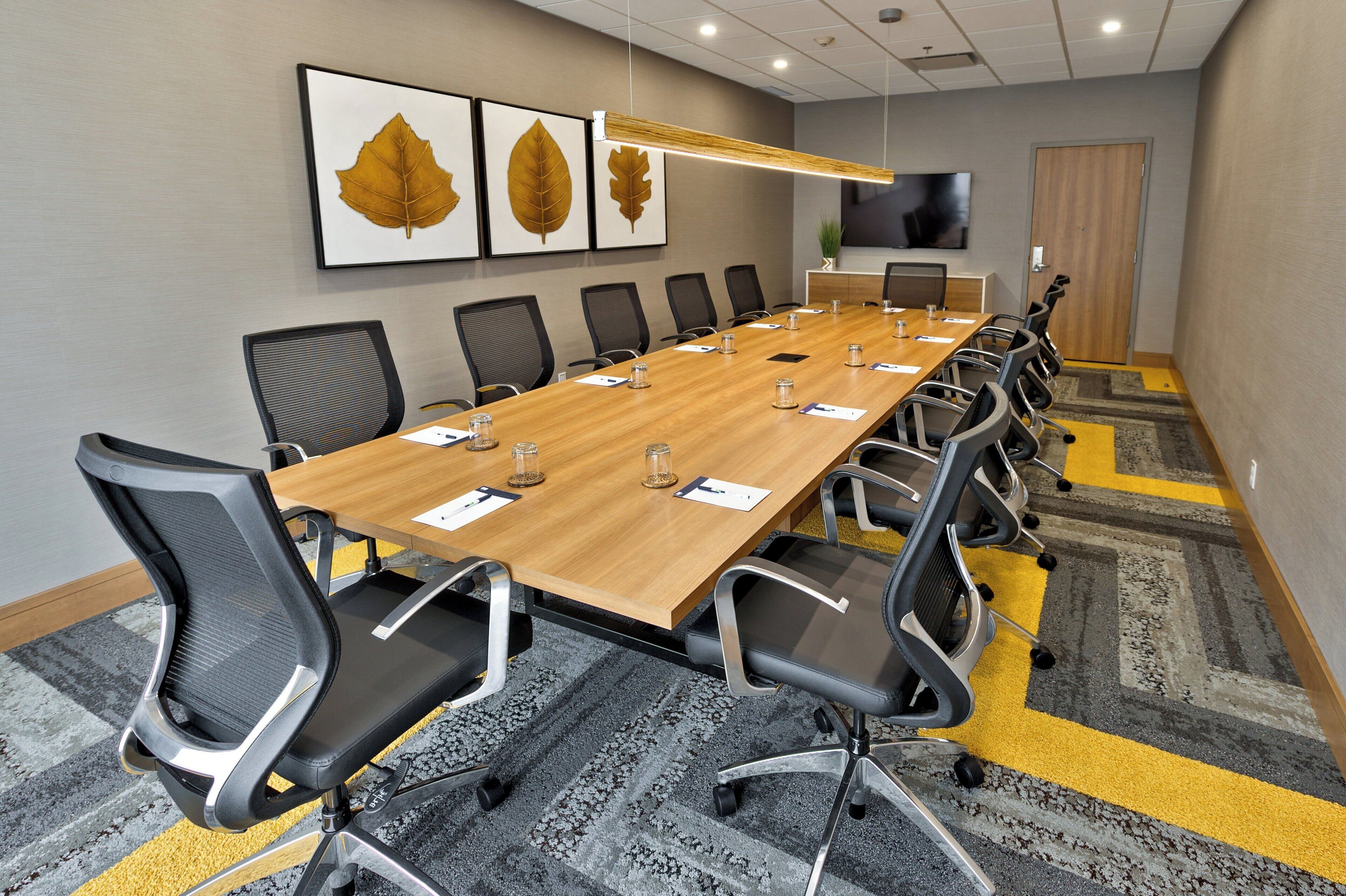 A conference room with a long table, chairs, and framed artwork on the wall.