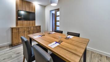 A conference room with a wooden table, four chairs, a television mounted on a wooden panel, and a door with frosted glass panels.