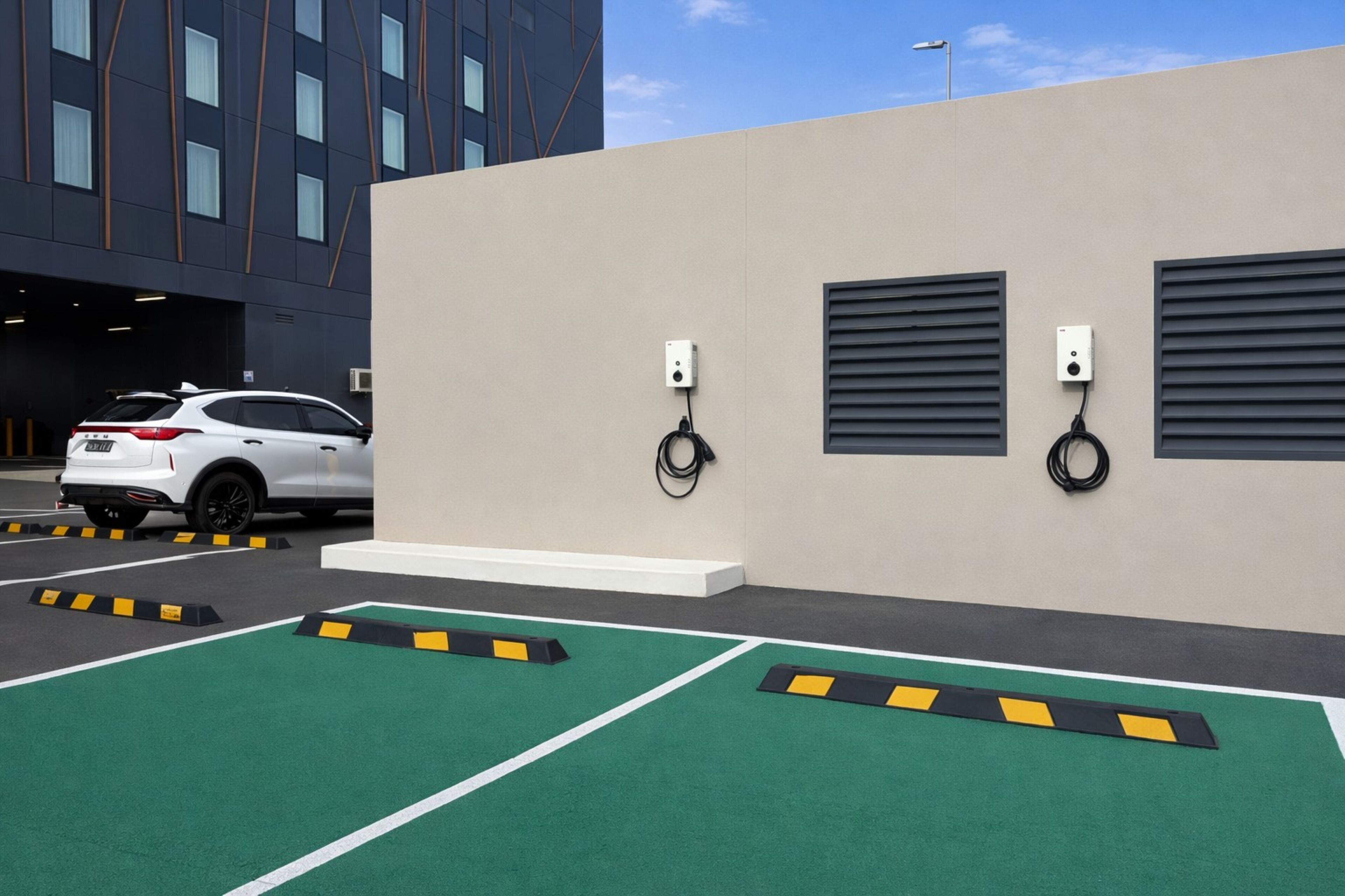 A parking area with electric vehicle charging stations, a white SUV, and a building with windows in the background.