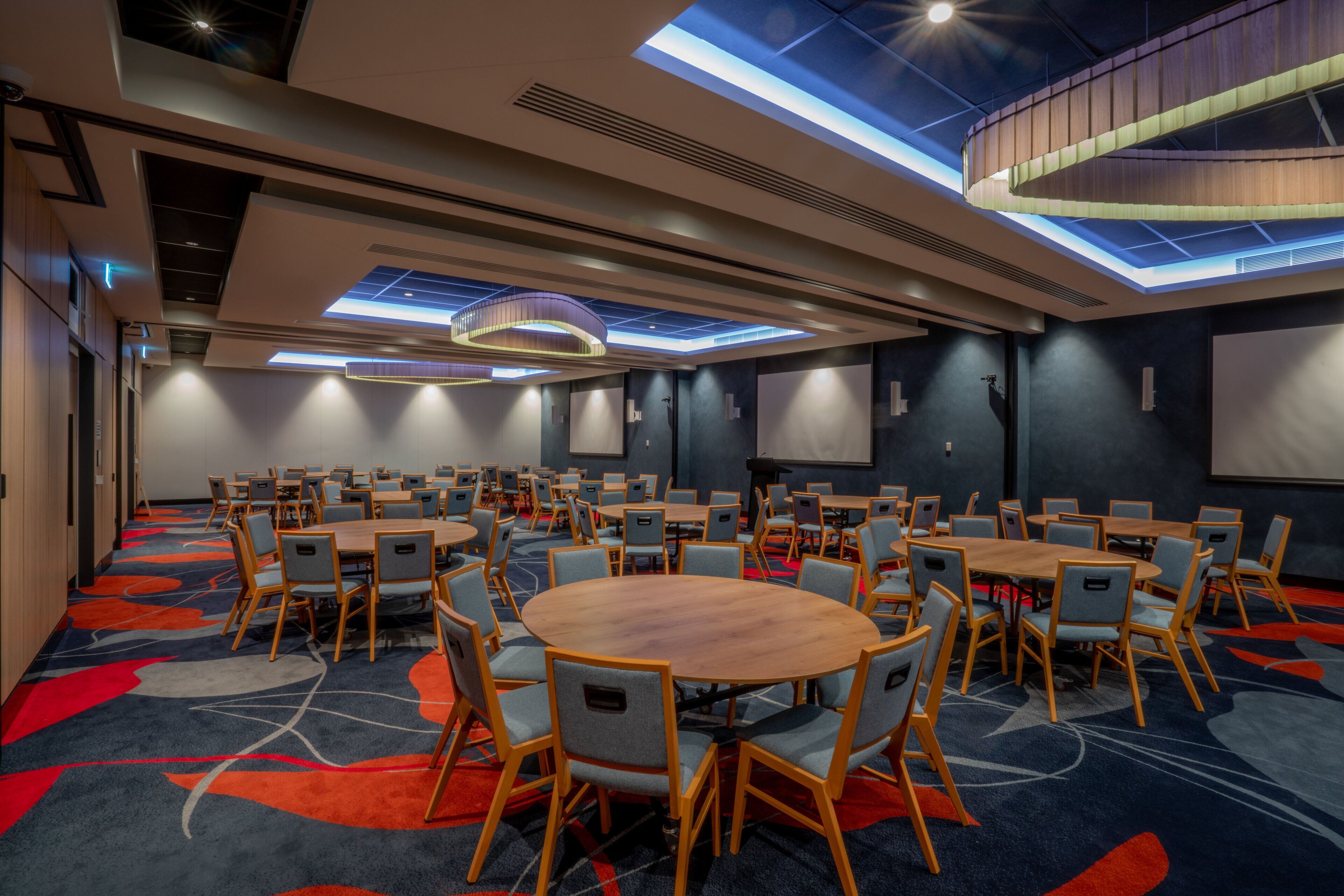 A conference room with multiple tables and chairs, a large screen, and a ceiling with skylights.