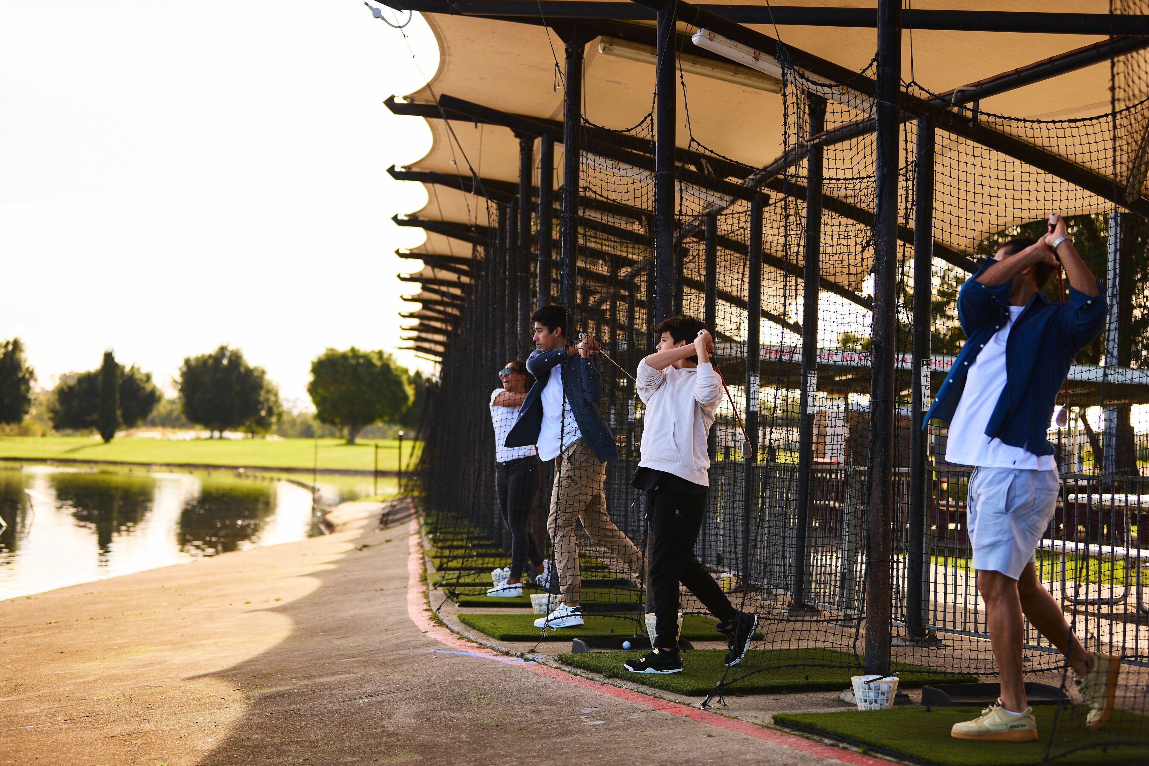 A group of people standing in a netted enclosure, possibly at a sports facility.