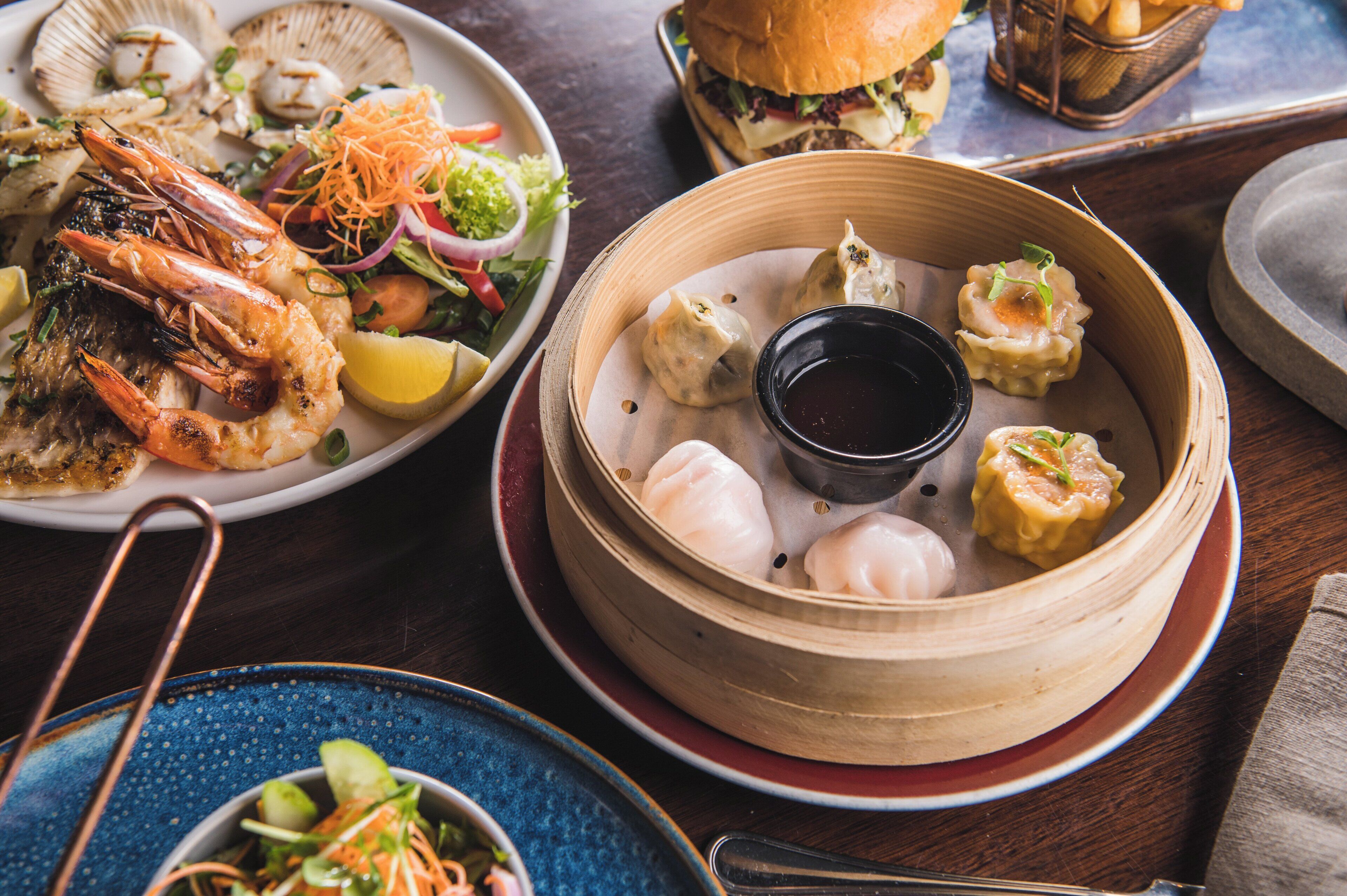 A variety of dishes including shrimp, dumplings, and a salad on a wooden table.