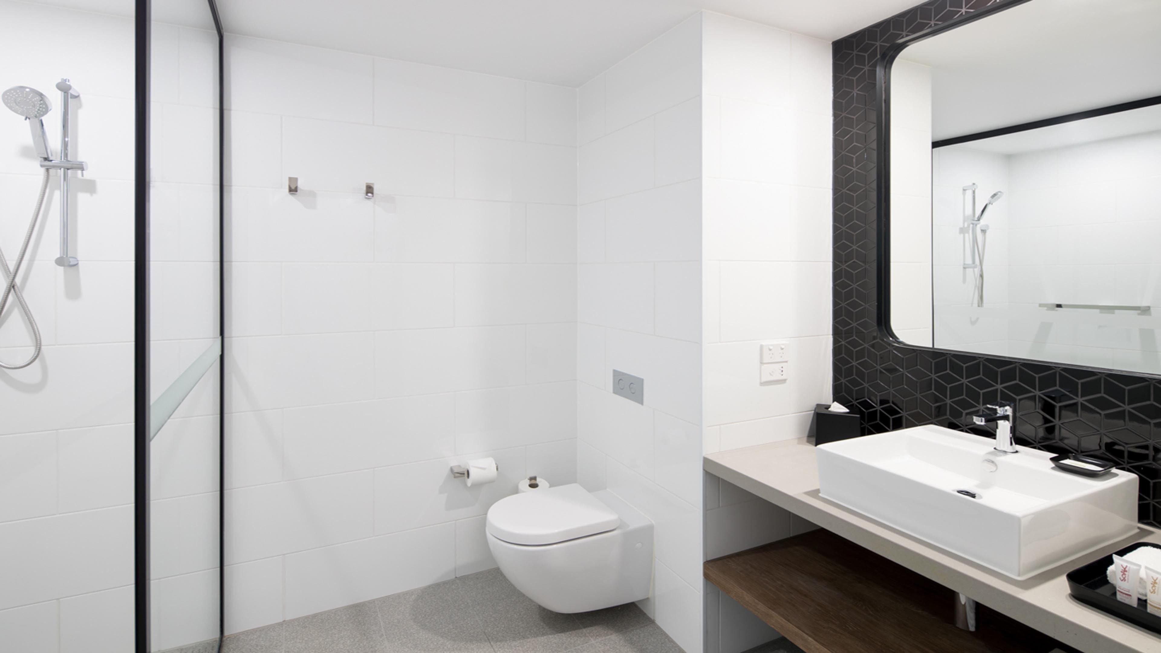 A modern bathroom with a white toilet, a shower area, and a vanity with a large mirror.