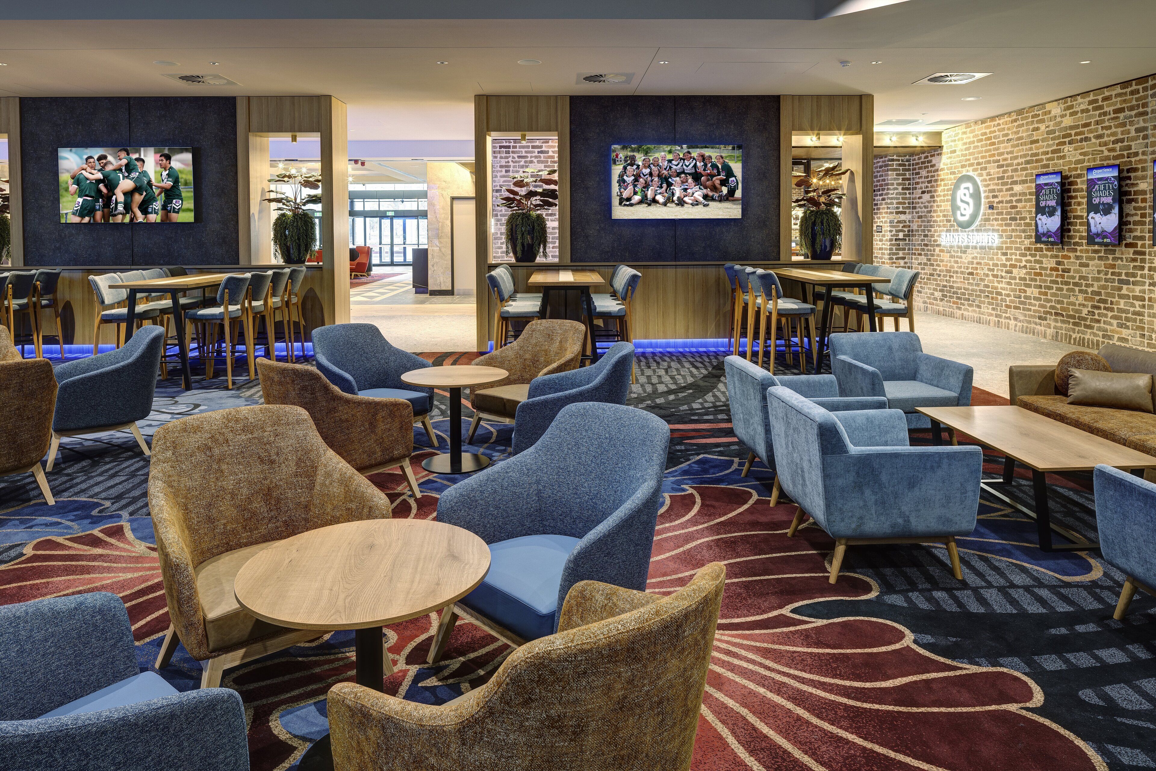 A hotel lobby with seating areas, a TV screen, and a brick wall.