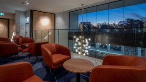 A modern hotel lobby with orange seating, a large glass wall with a city view, and a decorative light fixture. - Holiday Inn Sydney St Marys by IHG (North St Marys)