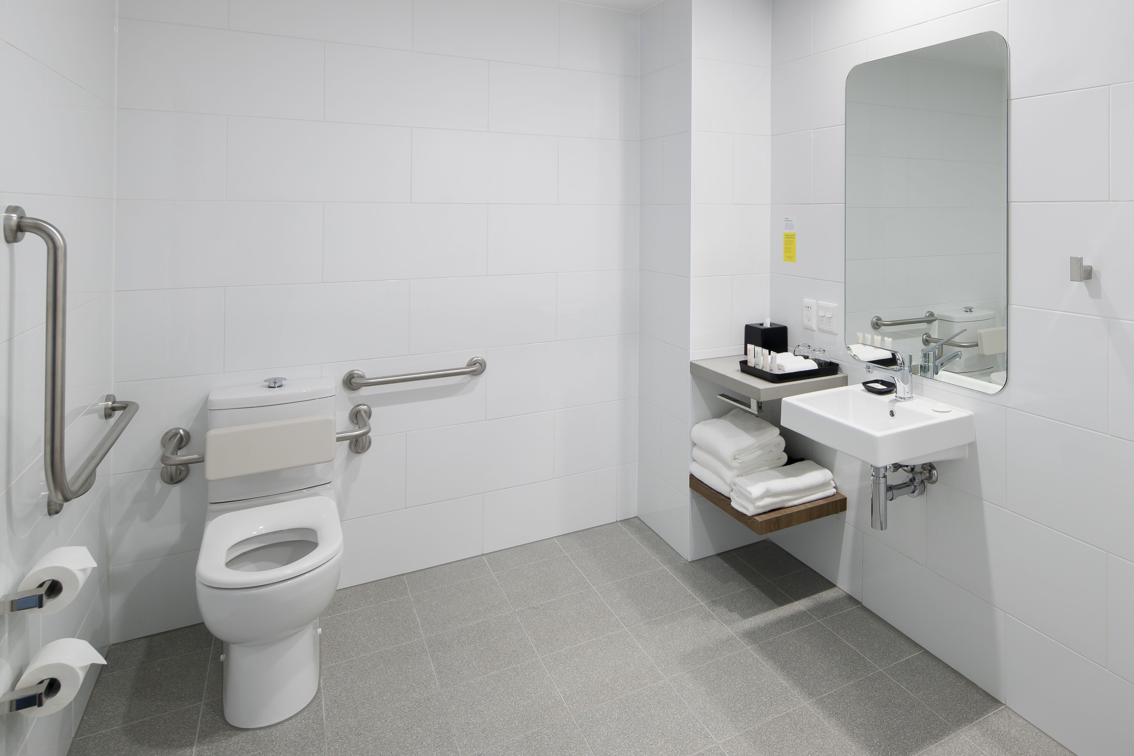 Un baño moderno con inodoro, barras de apoyo, lavamanos y espejo.