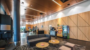 A modern lobby with a sofa, two round tables, a vending machine, and a reception desk. - Holiday Inn Sydney St Marys by IHG (North St Marys)