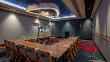 Un salón de conferencias con una larga mesa, sillas y un diseño moderno del techo.