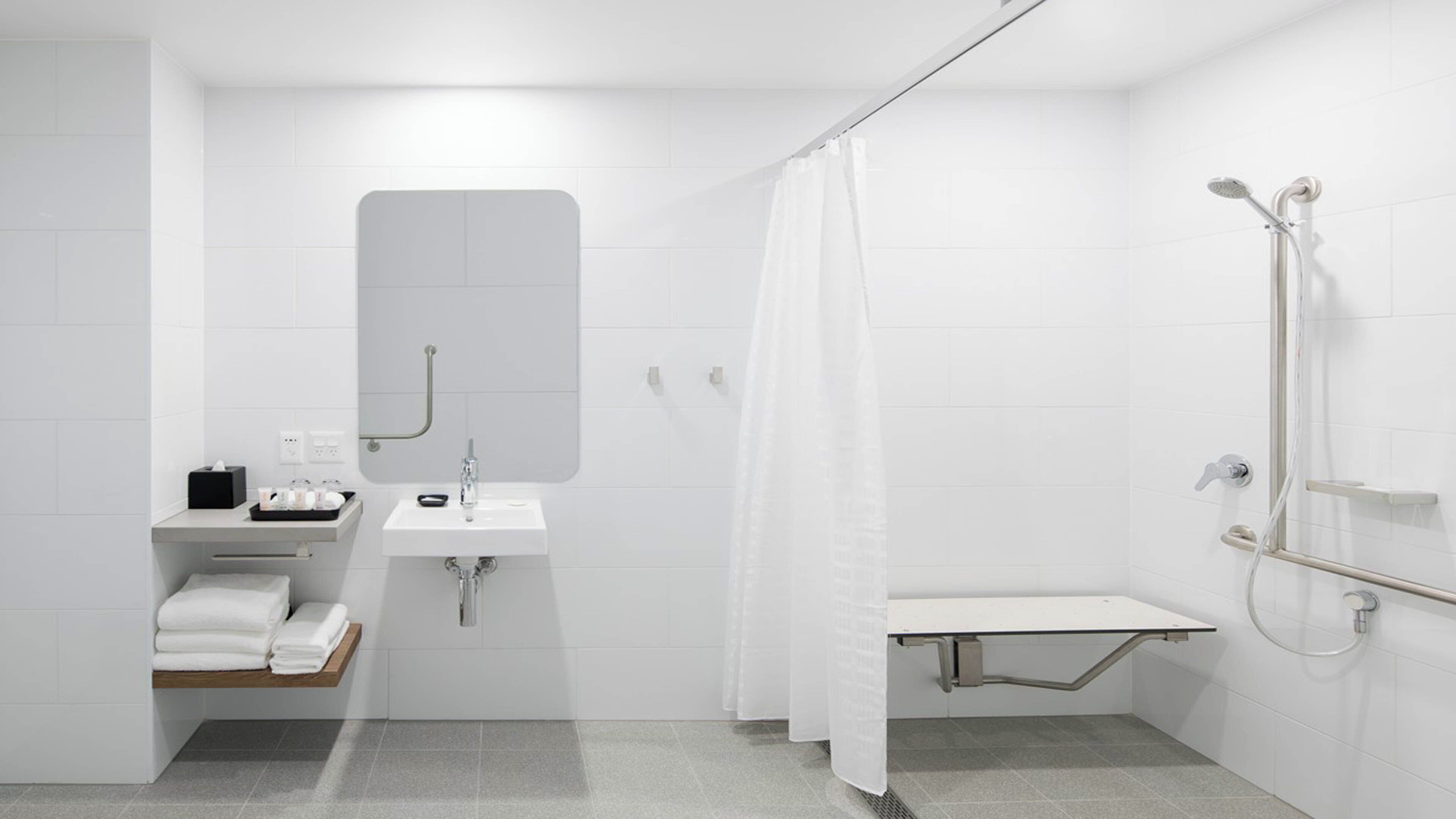 A modern bathroom with a sink, mirror, shower, and towel rack.