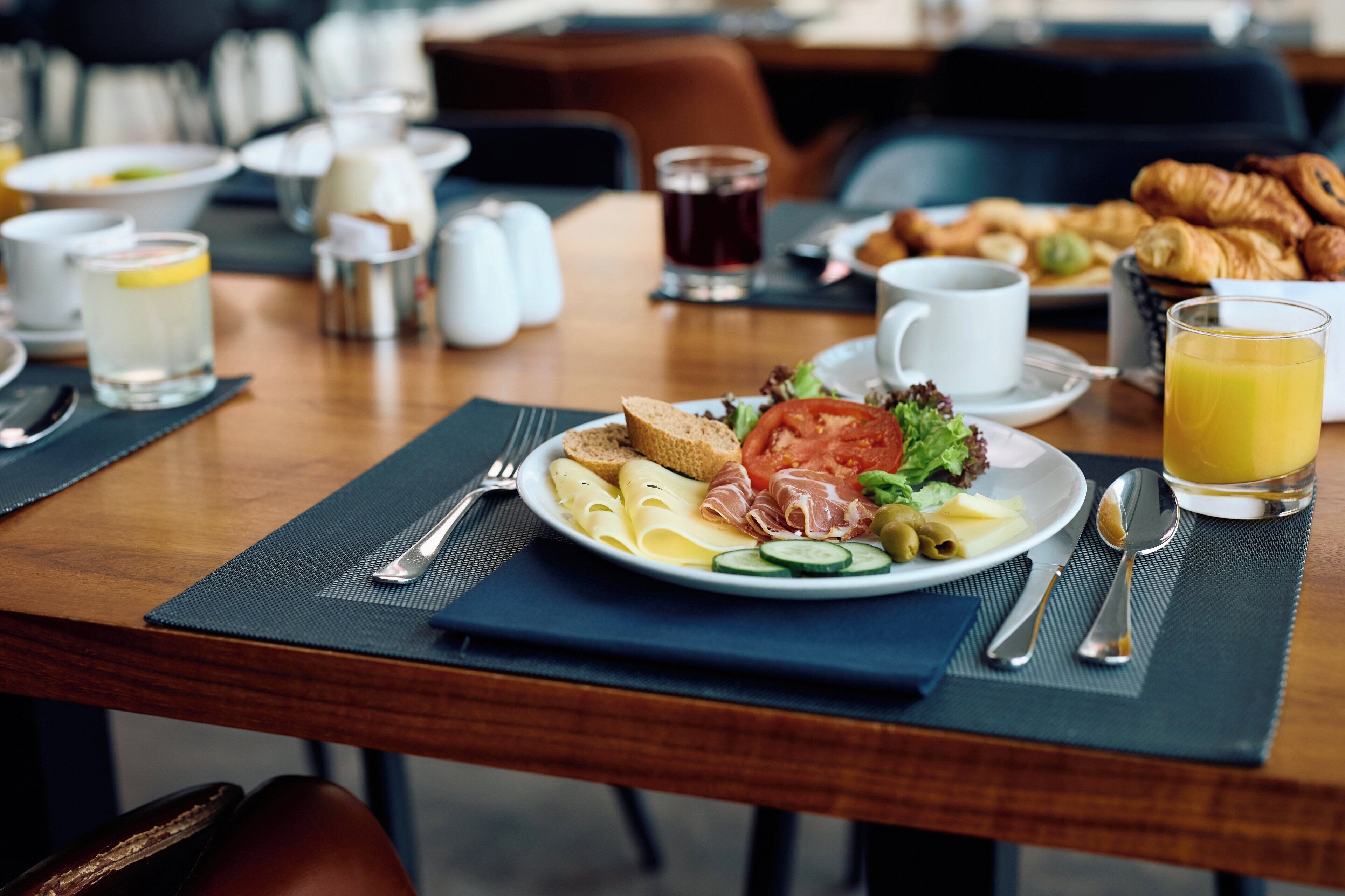 A breakfast table with a plate of food, including bread, cheese, and vegetables, and a glass of orange juice.