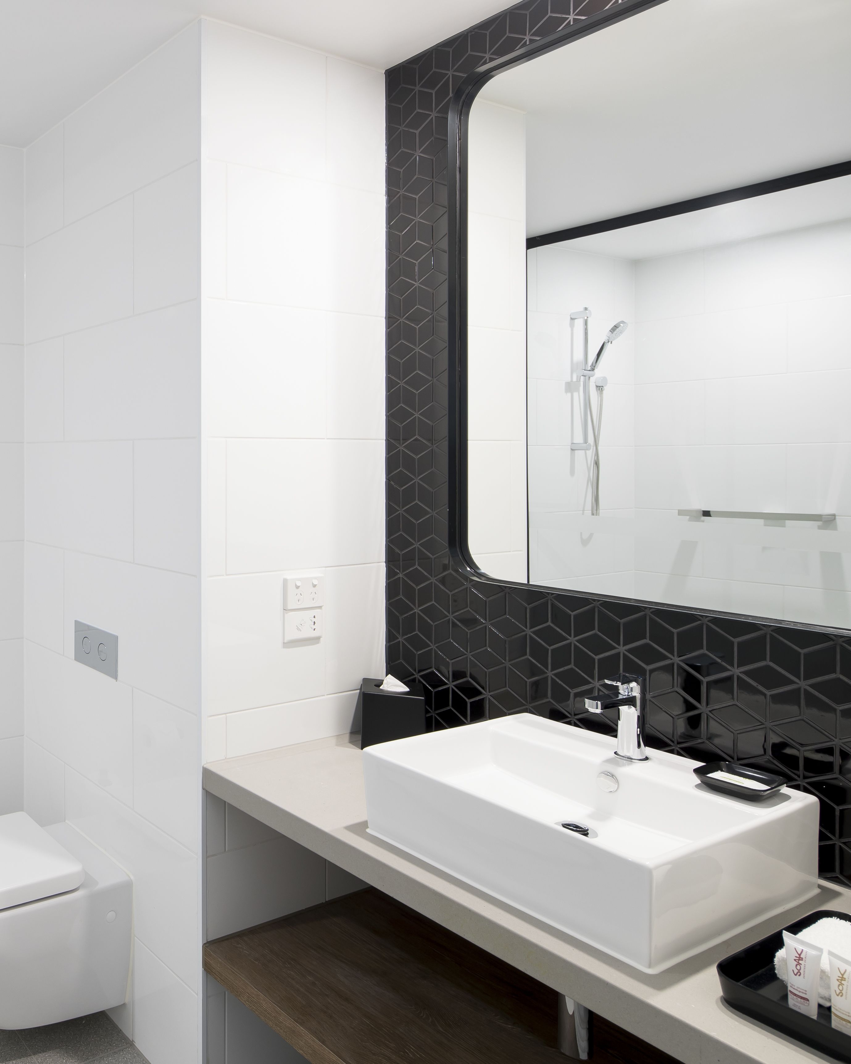 Un baño moderno con un lavabo blanco, una cabina de ducha con azulejos negros y un espejo grande.