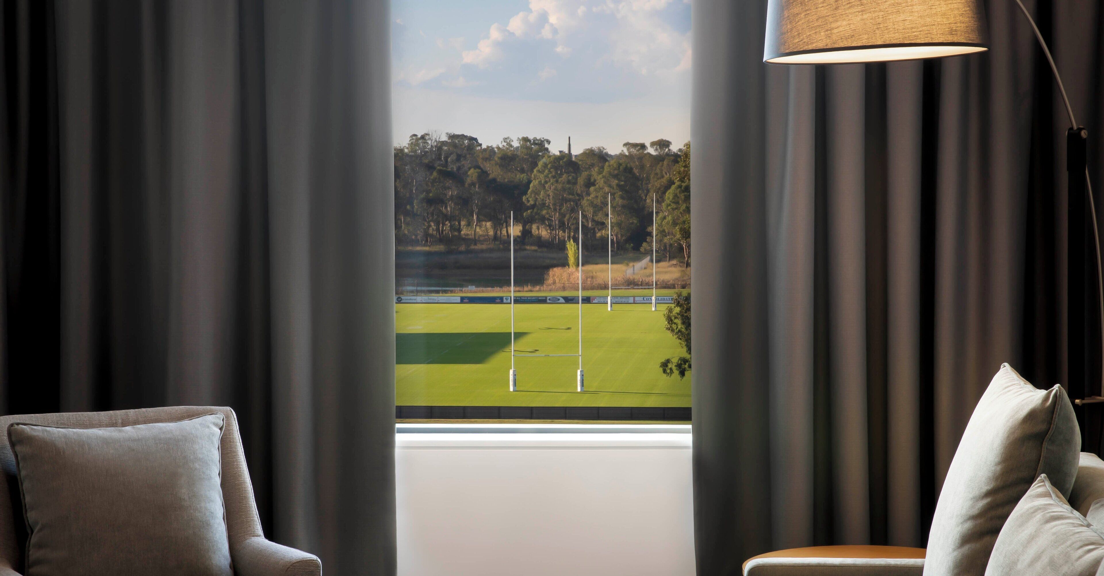 A room with a view of a golf course through a window with curtains.