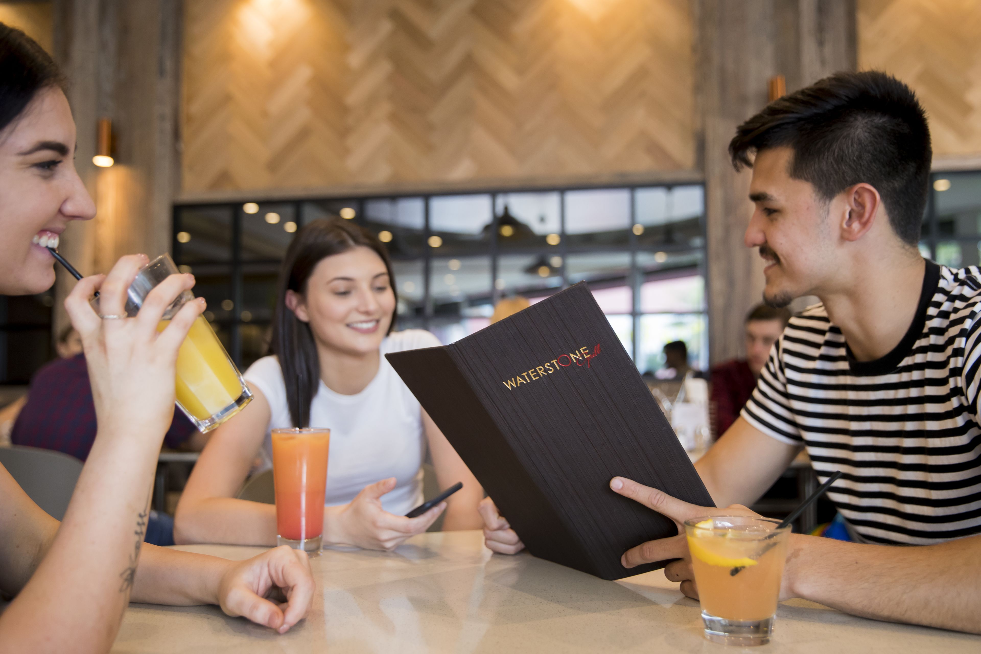 Een groep mensen zit aan een tafel in een restaurant met een modern interieur, waaronder een visgraatmotief op de muren en hanglampen.