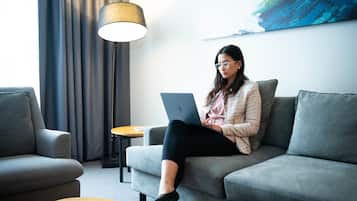 Eine Person sitzt auf einem grauen Sofa mit einem Laptop, einer Lampe und einem Gemälde an der Wand.