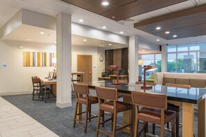 A modern interior with a central dining area, a reception desk, and a seating area with a view. - Holiday Inn Express and Suites San Marcos South by IHG (San Marcos)