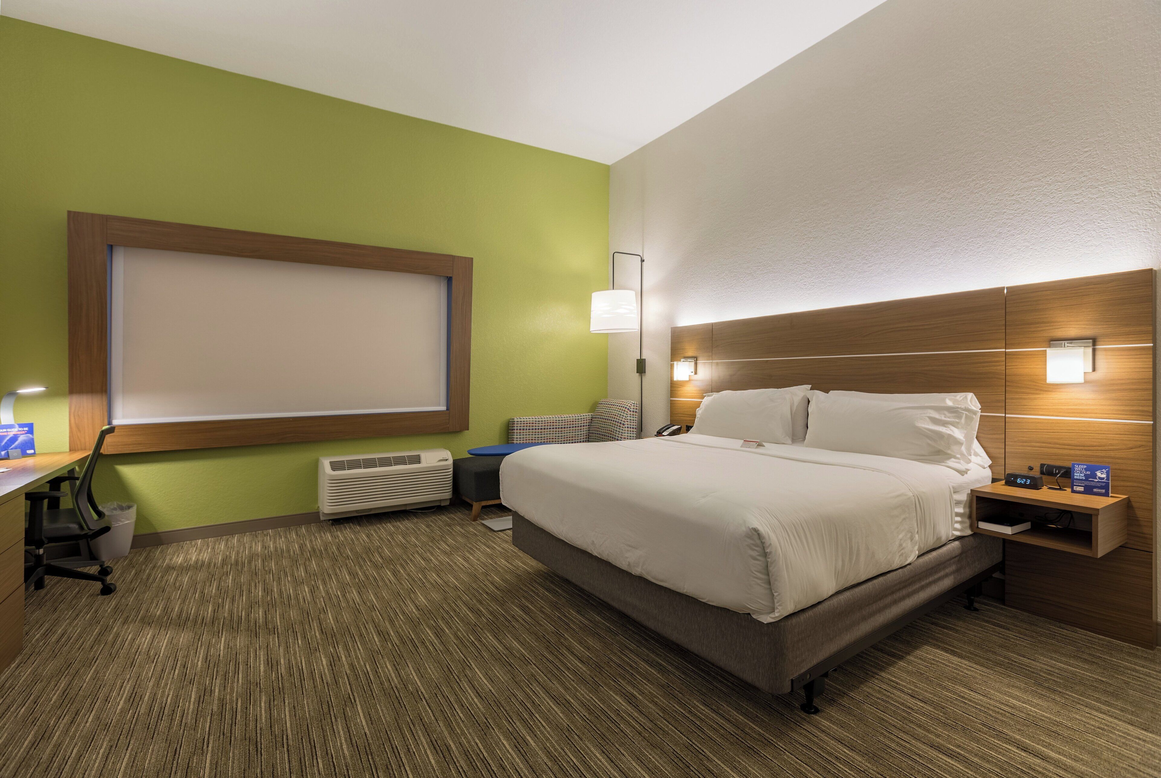 A hotel room with a bed, bedside table, lamp, and a desk with a chair.