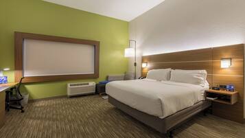 A hotel room with a bed, bedside table, lamp, and a desk with a chair.