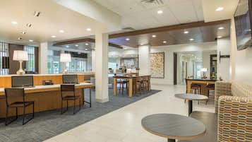 A hotel lobby with a reception desk, seating area, and a dining space.
