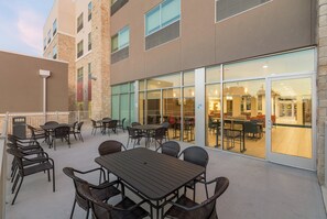 An outdoor patio with tables and chairs, a building with large windows, and a stone facade. - Holiday Inn Express and Suites San Marcos South by IHG (San Marcos)