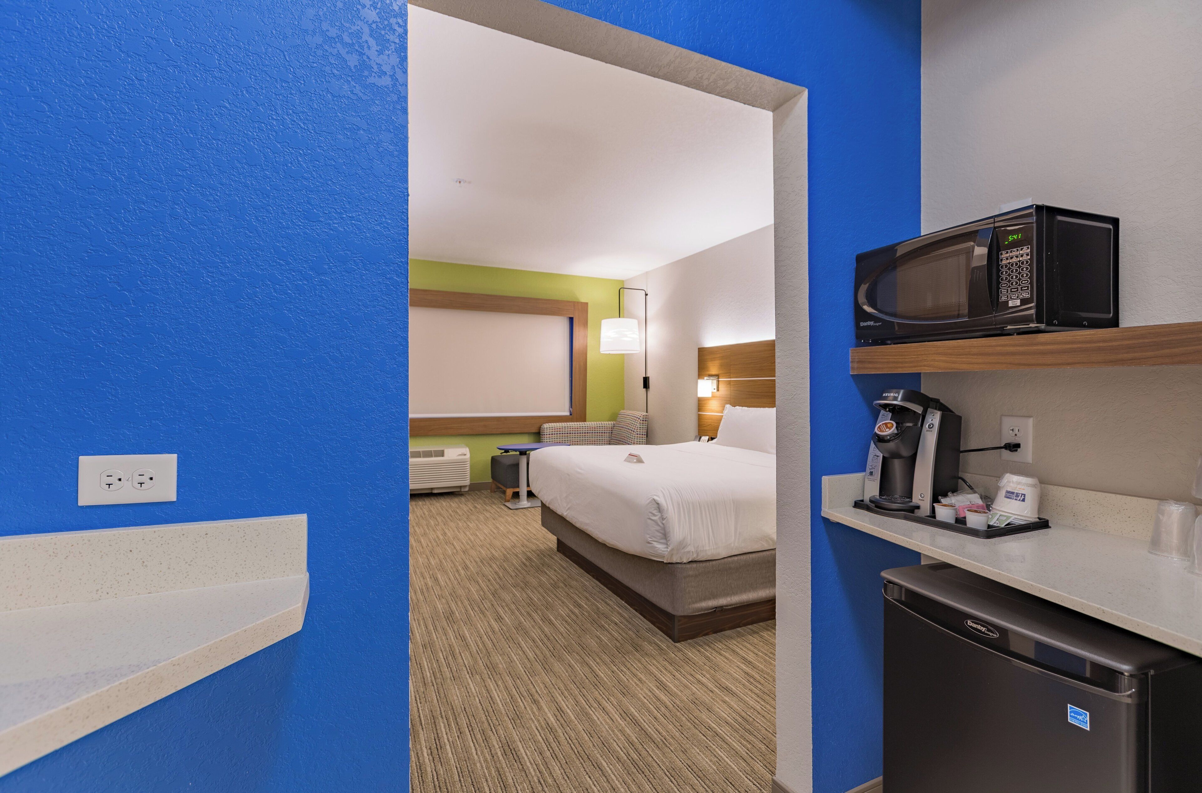 A hotel room with a bed, a microwave, a coffee maker, and a small refrigerator.