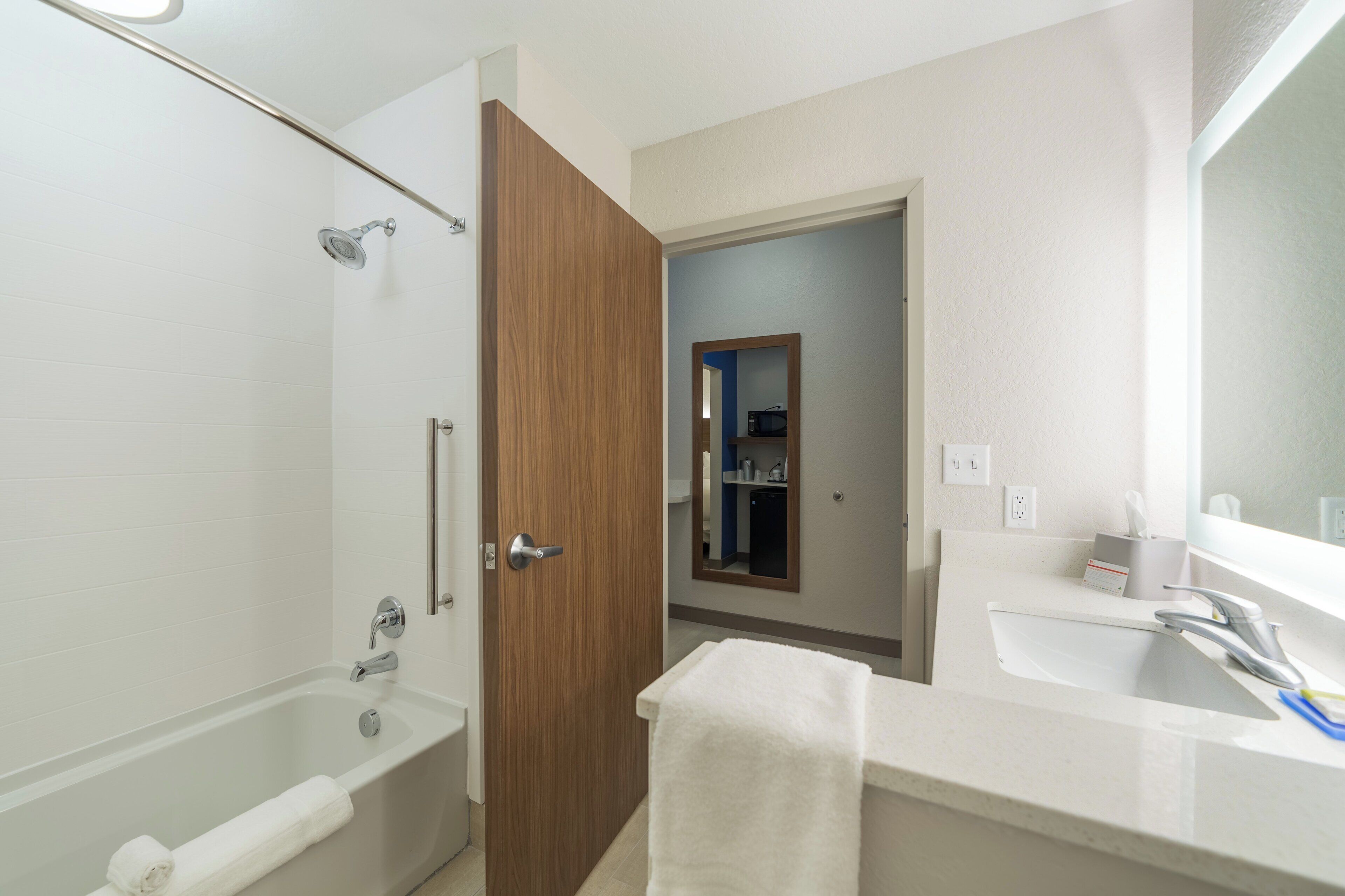 A bathroom with a bathtub, a wooden door, a mirror, and a sink.