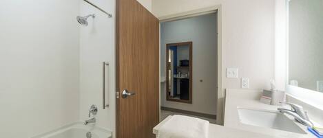 A bathroom with a bathtub, a wooden door, a mirror, and a sink.