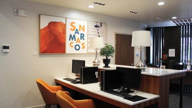 A modern hotel lobby with a reception desk, multiple computer stations, and orange chairs. - Holiday Inn Express and Suites San Marcos South by IHG (San Marcos)