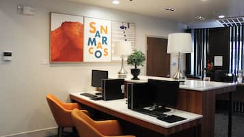A modern hotel lobby with a reception desk, multiple computer stations, and orange chairs.