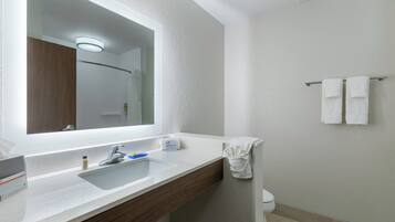 Un baño con un espejo grande, un lavamanos, un perchero para toallas y un inodoro.
