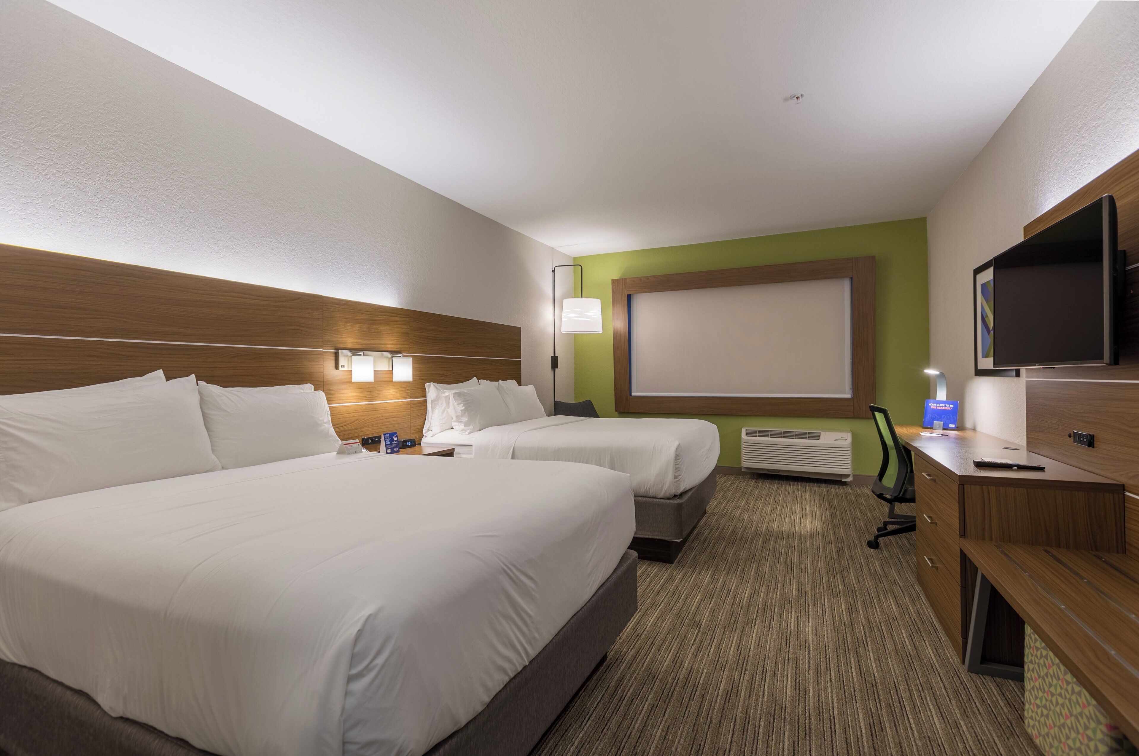 A hotel room with two beds, a desk, a TV, and a large window.