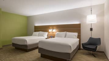 A hotel room with two beds, a desk, a chair, and a lamp.