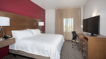 A hotel room with a bed, a desk with a lamp, a chair, a television, and a window with curtains.