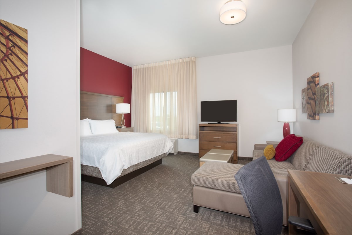 Una habitación de hotel con una cama, un escritorio, una silla, un televisor y un sofá.