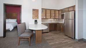 Habitación de hotel pequeña con kitchenette, una cama, zona de comedor con mesa y sillas, y un cuadro pequeño en la pared.